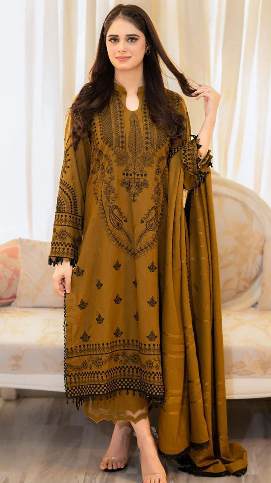 Woman wearing a mustard yellow traditional outfit with black patterns in a well-lit room.